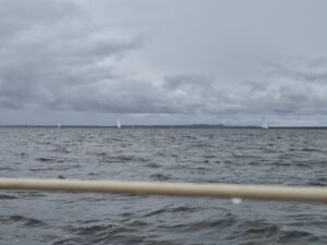 Über die Reling eines Bootes aufs Haff fotografiert. In einigem Abstand sieht man mehrere Segelboote.