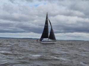 Ein Segelboot mit dunklem Groß- und Vorsegel auf dem Wasser.